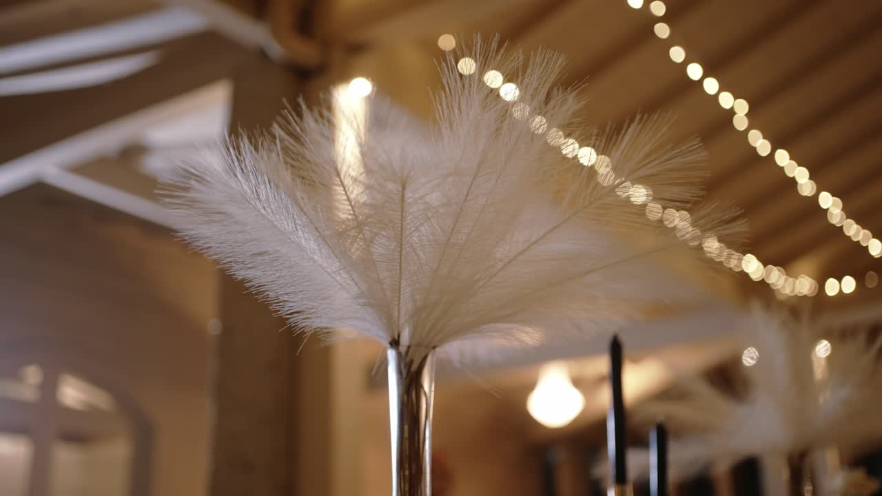 White feather centerpiece in tall vase with glowing string lights in soft background