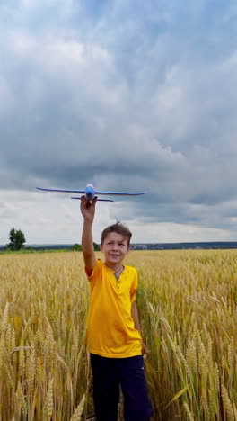 little boy on yellow field. happy child playing outdoors in summer. kid holds a toy plane and imitate flight over the meadow. front view. vertical video
