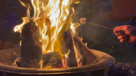 Static-shot-of-a-camp-fire-burning-with-people-sitting-round-cooking-marshmellows