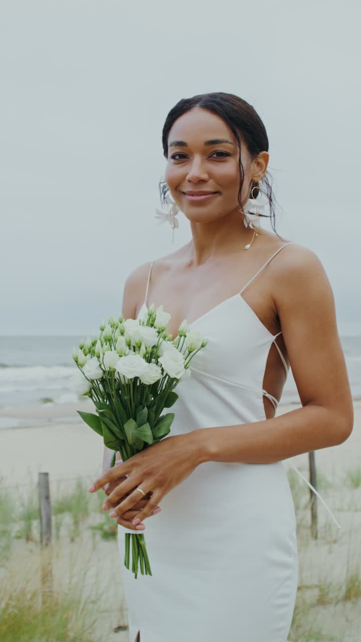 Donna in abito bianco che tiene un bouquet sulla spiaggia