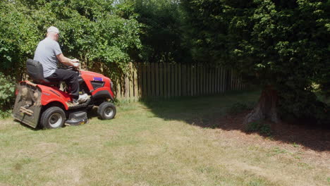 a man cutting grass on a ride on lawn mower along a fence line in a garden