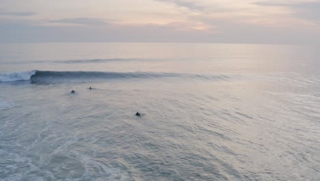 Surfers-paddling-out-to-waves-in-tropical-waters,-sunset-aerial-panoramic-view
