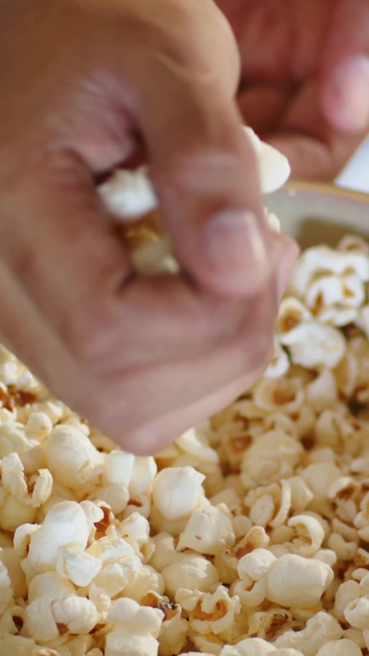 Video verticale: Una mano che si allunga per prendere popcorn da una grande ciotola su un tavolo di legno, prendendo uno spuntino.