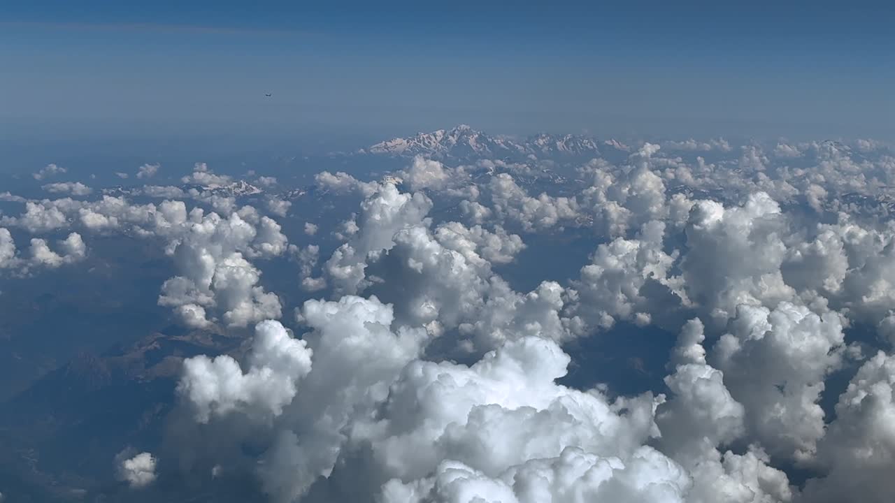 An elevated pilot perspective while flying in a summer morning over cottony white cumulonimbus clouds, with the Montblanc Peak at the back, under a blue sky.