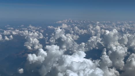 an elevated pilot perspective while flying in a summer morning over cottony white cumulonimbus clouds, with the montblanc peak at the back, under a blue sky.