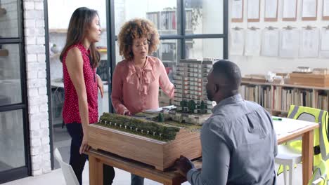 Busy-diverse-colleagues-discussing-work-over-city-model-on-table-in-office-in-slow-motion