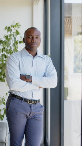 vertical video: confident businessman standing with arms crossed near window in office