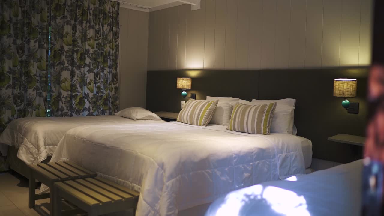 Camera d'albergo confortevole con letti matrimoniali e singoli, eleganti luci da comodino e tende floreali di stile, creando un'atmosfera calda e accogliente per gli ospiti