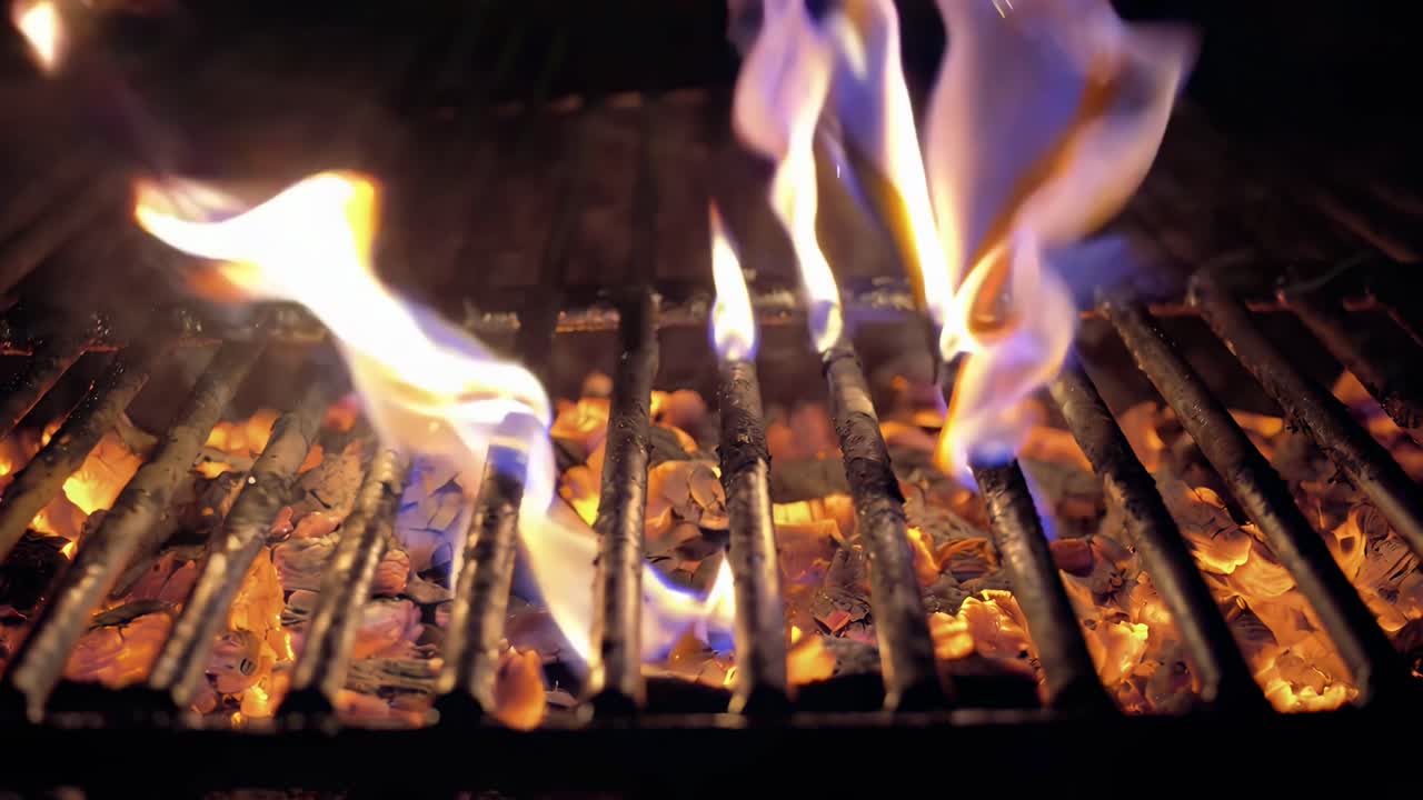 Video en primer plano de llamas que se elevan a través de una parrilla, capturado desde un ángulo bajo, creando una atmósfera cálida y dinámica.