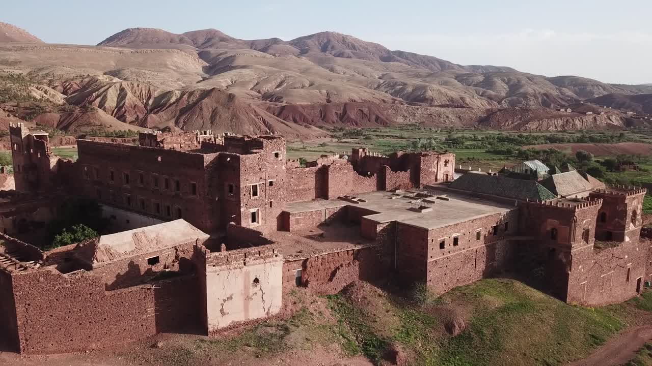Ilmakuva linnoitetusta marokkolaisesta kasbahista Ouarzazatessa, jota ympäröivät Atlasvuoret ja vihreä laakso. Vahva historiallinen arkkitehtuuri, ihanteellinen perintökohteeksi, matkailuun ja elokuvatuotantoihin.