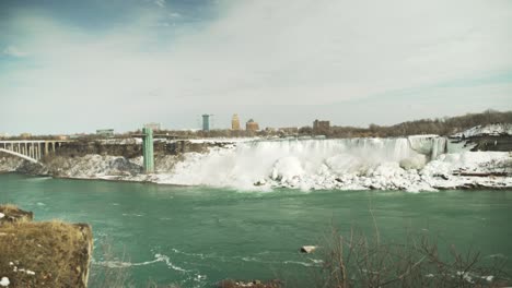 Cataratas-Del-Niágara-Heladas-Desde-El-Otro-Lado-Del-Agua-En-Invierno,-Toma-Amplia-De-Mano