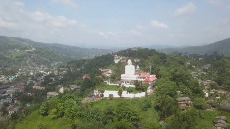 Hilltop-Buddha-sculpture-in-humid,-hazy-Kandy-Sri-Lanka,-aerial-view