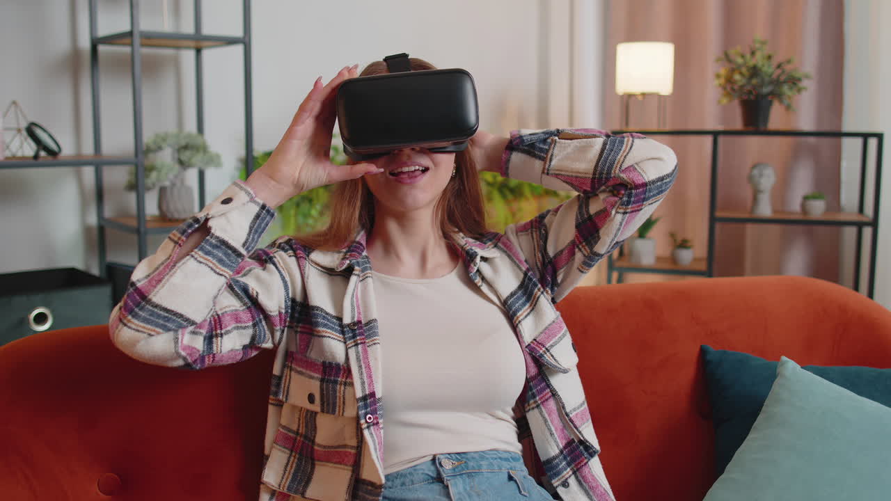 una mujer joven usa gafas de realidad virtual en casa, disfrutando del concepto de video moviendo las manos en el aire