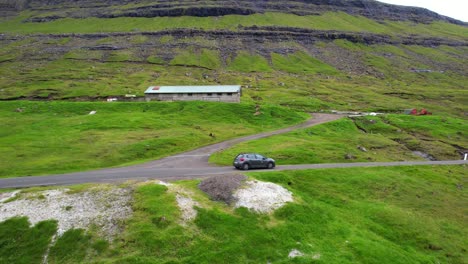 drone tracking a car driving to saksun in a road surrounded by mounts and waterfalls in faroe islands