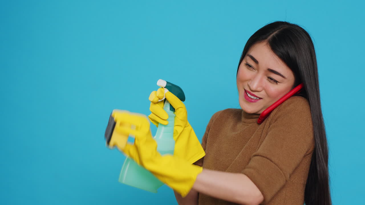 Asian housekeeper using duster and protective gloves to clean house