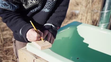 un hombre está inscribiendo detalles en una pequeña tabla de madera para la bañera de baño caliente diy - cerca