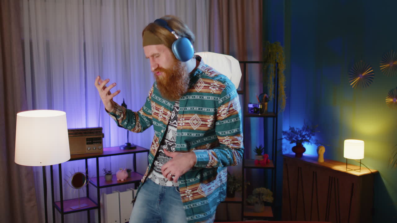 헤드폰을 착용한 남자가 소파에서 춤을 추고 집에서 좋아하는 음악을 듣고 상상의 기타를 연주하고 있습니다.