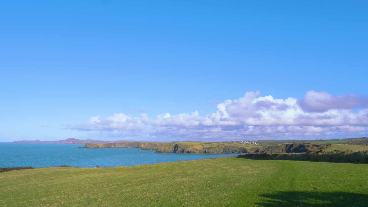 Beautiful Wide Landscape of Welsh Coastline in Pembrokeshire with Blue Sky and Clouds with Big Open Field and Clear Sea Water 4K.