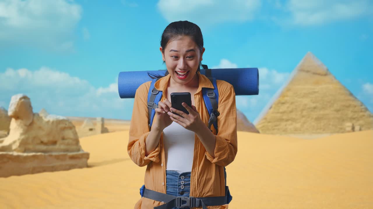 Asian Female Hiker With Mountaineering Backpack Looking At The Smartphone And Saying Wow While Traveling In Pyramid Of Giza