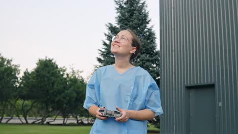 Woman-enjoys-flying-the-drone-using-the-remote-controller-while-watching-over-it,-handheld-static