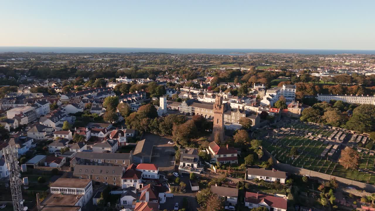 Very high drone footage over St Peter Port Guernsey showing houses and buildings including the Arsenal, Fire Station and cemetery in late afternoon sun