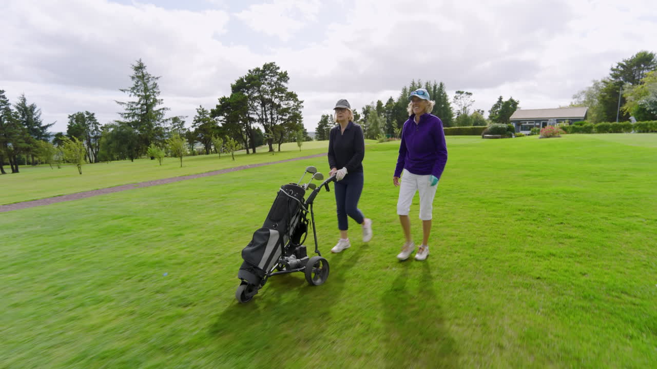 Female golf players walking with clubs and talking on golf course on cloudy day
