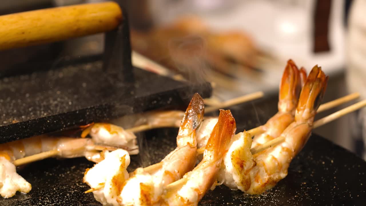 Close-up of shrimp skewers sizzling on a griddle, showcasing their golden-brown texture.