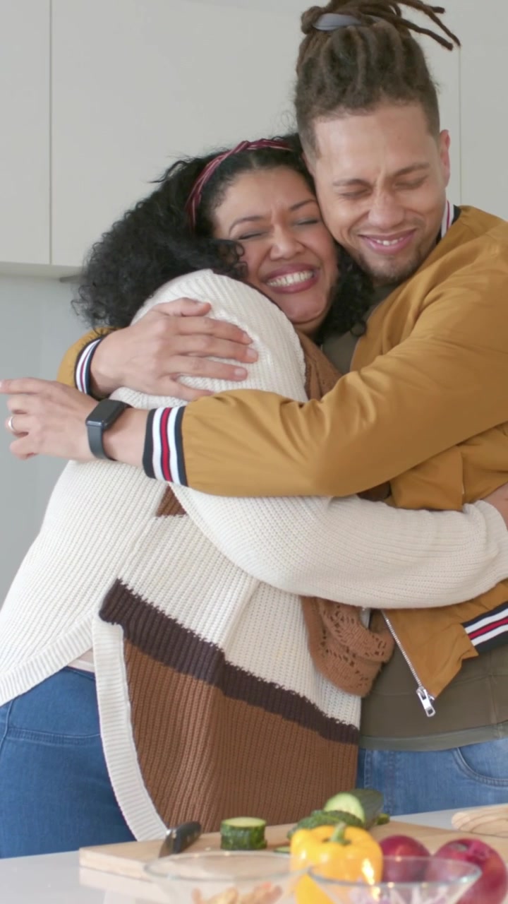 Video verticale: Donna in maglione che si muove, toccando il braccio e appoggiata all'isola della cucina, mentre un uomo la abbraccia sorridendo.
