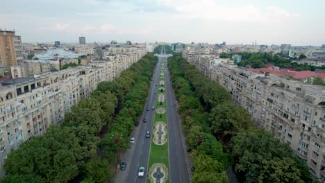 aerial view of unirii boulevard, near unirii square in bucharest, romania surrounded by tall apartment building, lush vegetation and beautiful water fountains, city center, traffic, backwards movement