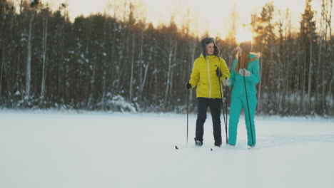 a man in a yellow jacket and a girl in a blue jumpsuit skiing in slow motion at sunset