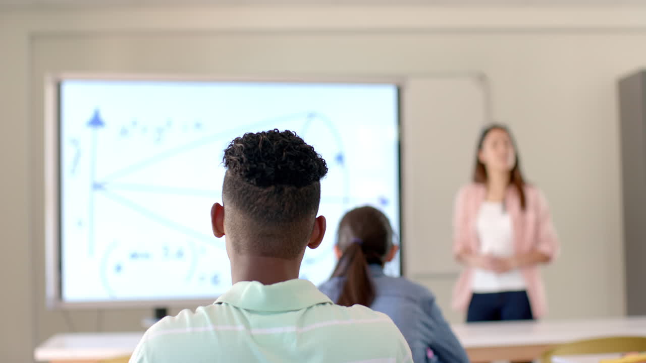 Teenage biracial boy raises his hand in a classroom at high school