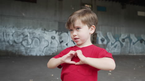 un niño pequeño se está divirtiendo y haciendo símbolos de corazón con las manos frente a la cámara en una camiseta roja