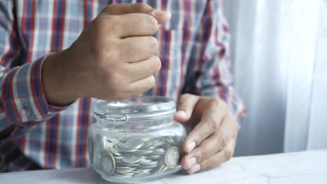 person putting coins in a glass jar