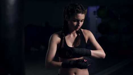 Woman-wrapping-hands-with-black-boxing-wraps-in-dark-room-and-taking-on-boxing-gloves.-Close-up-shot-in-4k