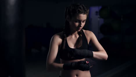 Mujer-Envolviéndose-Las-Manos-Con-Envolturas-De-Boxeo-Negras-En-Un-Cuarto-Oscuro-Y-Poniéndose-Guantes-De-Boxeo.-Primer-Plano-En-4k