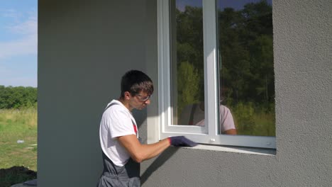 man worker in safety glasses cleaning surface for pvc window metal sill installation