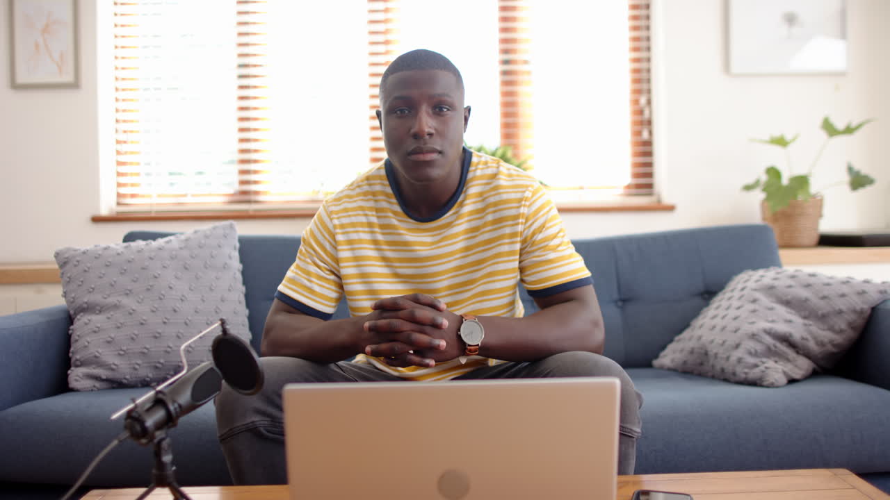 Sitting on couch, african american man with laptop and microphone, podcast recording, at home
