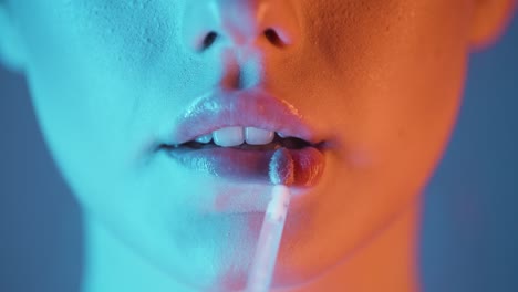 primer plano extremo de una mujer joven aplicando brillo de labios brillante en sus labios para labios hermosos y lisos con contraste naranja turquesa en su rostro en cámara lenta
