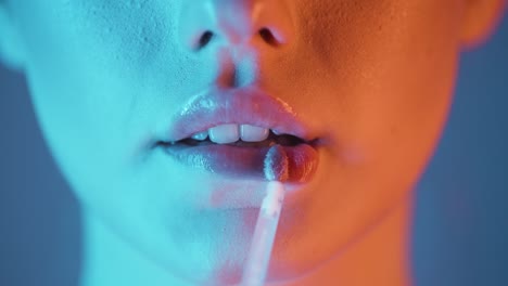 extreme close up of a young woman applying glossy lip gloss on her lips for beautiful looking and smooth lips with turquoise orange contrast on her face in slow motion