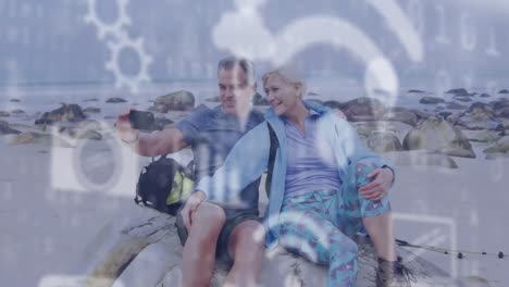 animación de iconos digitales en línea sobre una pareja de ancianos en la playa tomando selfies con teléfonos inteligentes