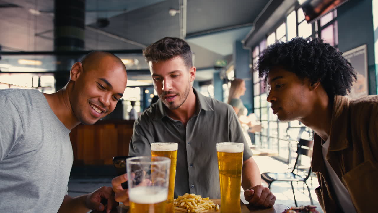 Group Of Male Friends Meeting Up In Bar Taking Photo Of Food On Mobile Phone