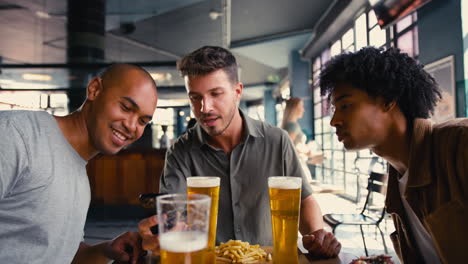 group of male friends meeting up in bar taking photo of food on mobile phone