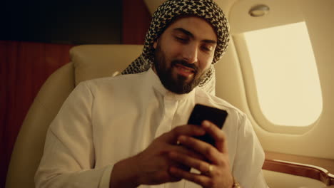 Smiling-businessman-chatting-online-in-airplane-closeup.-Muslim-businessman-hold