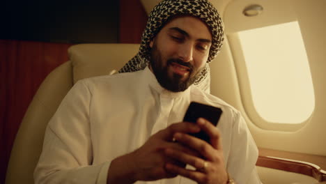 smiling businessman chatting online in airplane closeup. muslim businessman hold