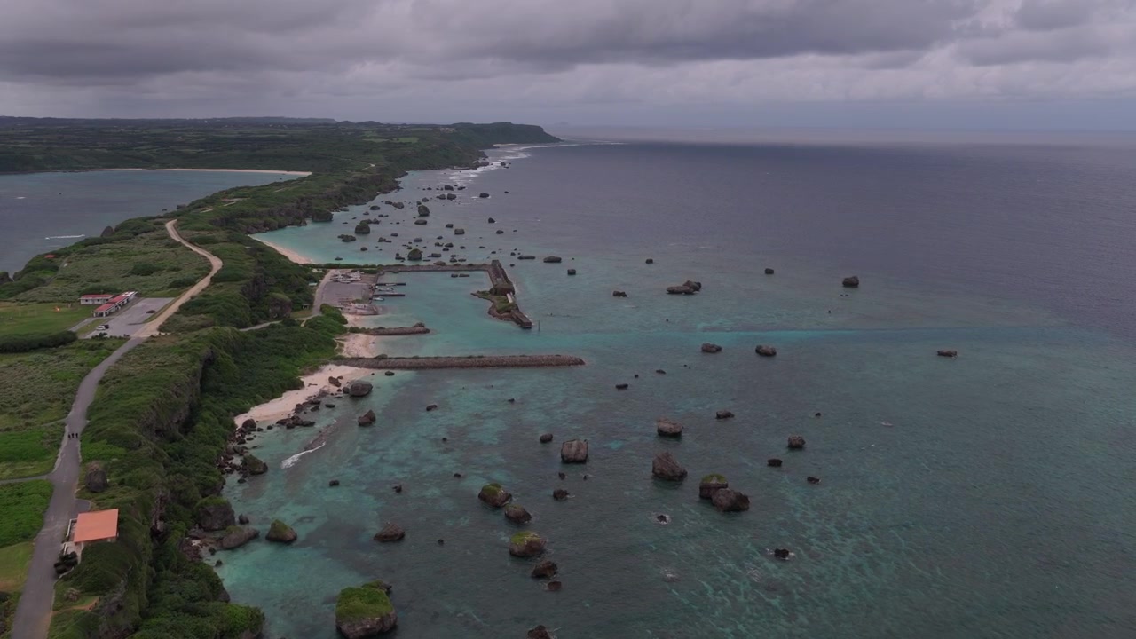 Japonya, Okinawa, Miyakojima'daki Hennasaki Deniz Feneri, Bora Balıkçı Limanı ve Maibah Plajı yakınlarındaki kayalık kıyı şeridi üzerinde ileri doğru hareket eden yatay havadan çekim.