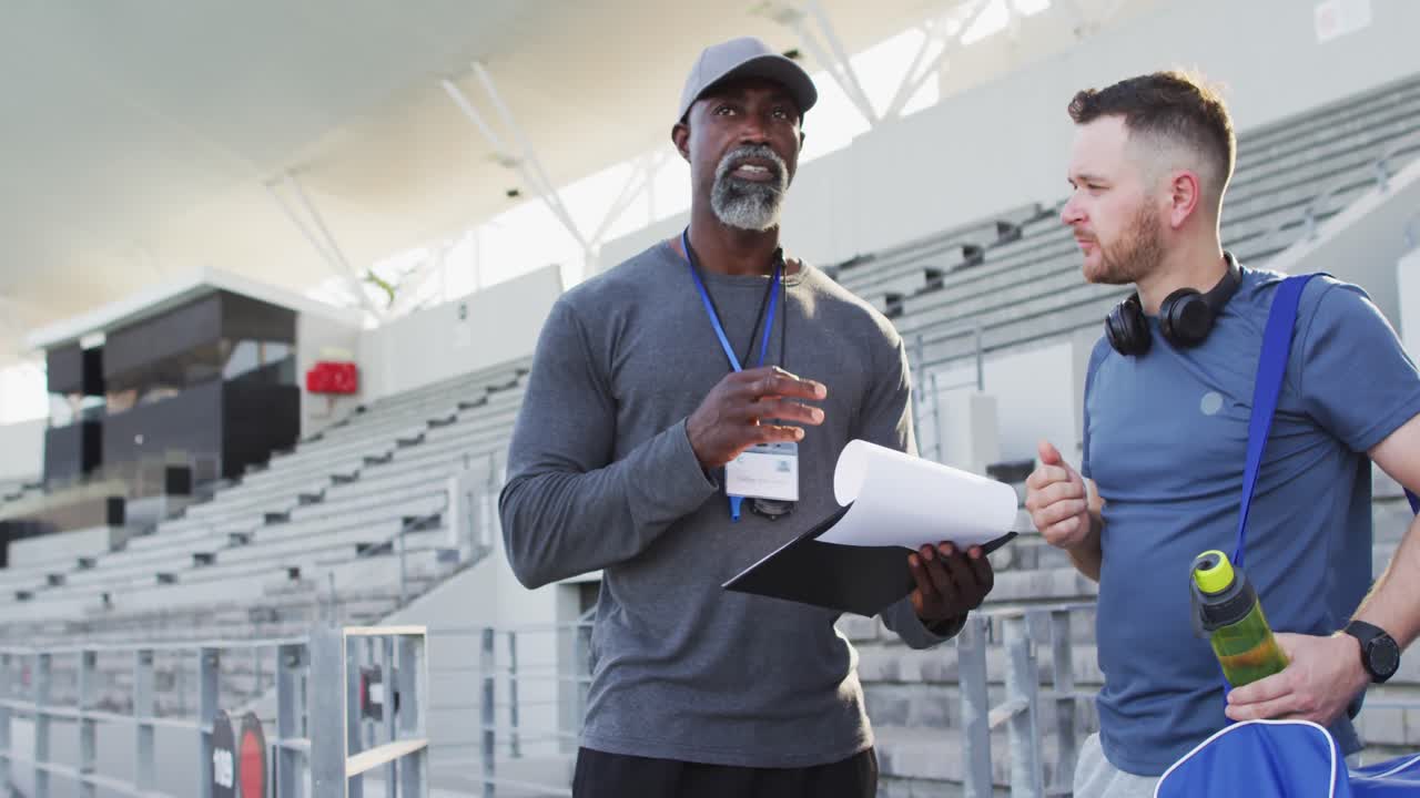 entrenador masculino afroamericano y atleta caucásico hablando durante una sesión de entrenamiento