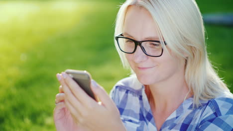 portrait of a young woman wearing glasses enjoying a smartphone in the park beautiful sun glare 4k s