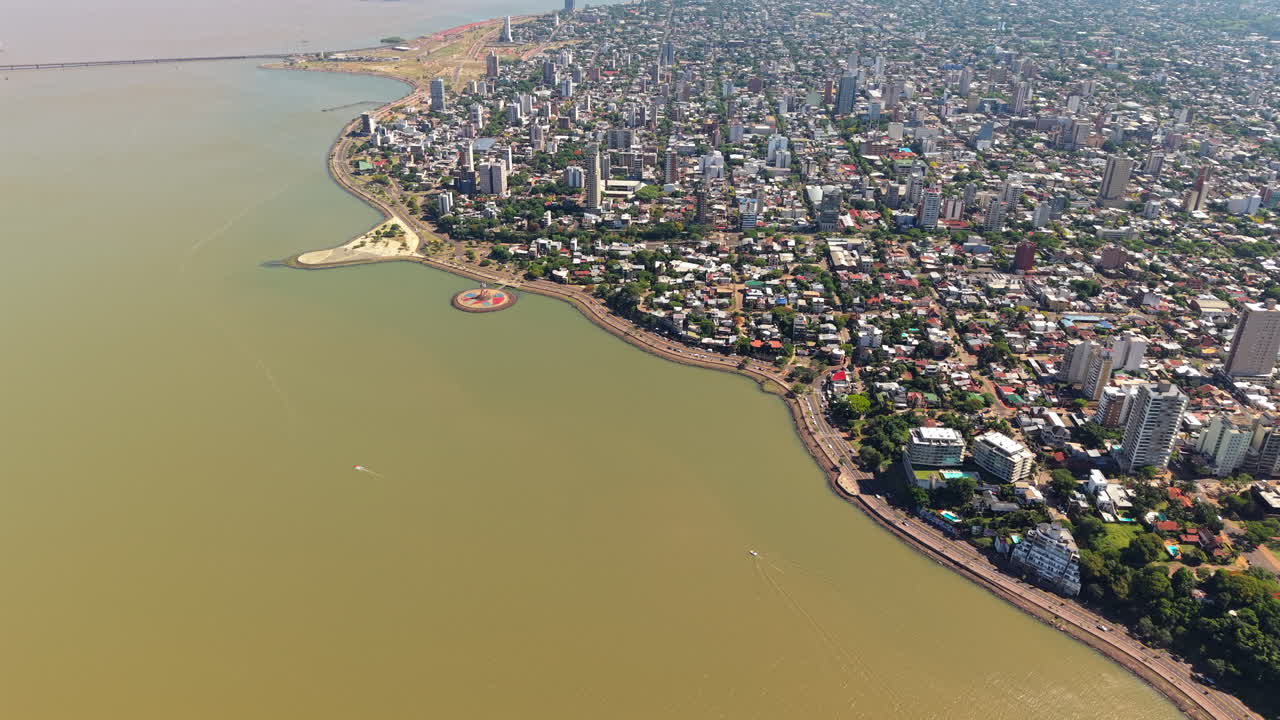 Aerial shot over the coast of the Parana River in Posadas, Argentina. Overflight of the city with its streets, houses and buildings on a sunny day.