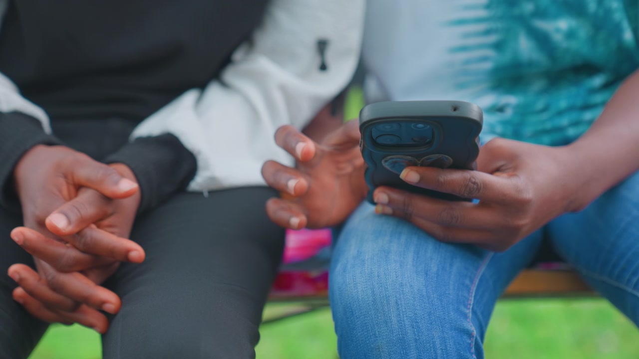 Black mother and child hands hold phone, closeup of intertwined fingers and device, textured denim and folded palms, thumb scrolling through notification, intimate gesture, nervous anticipation
