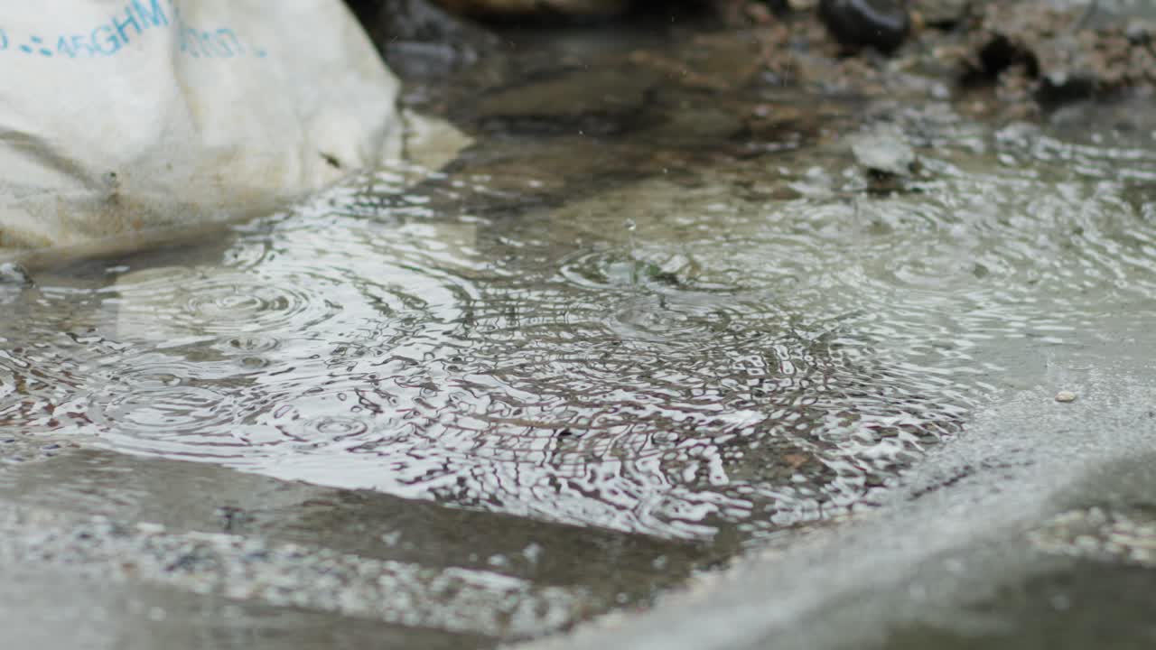 Raindrops create ripples on a wet sidewalk during a rainy day